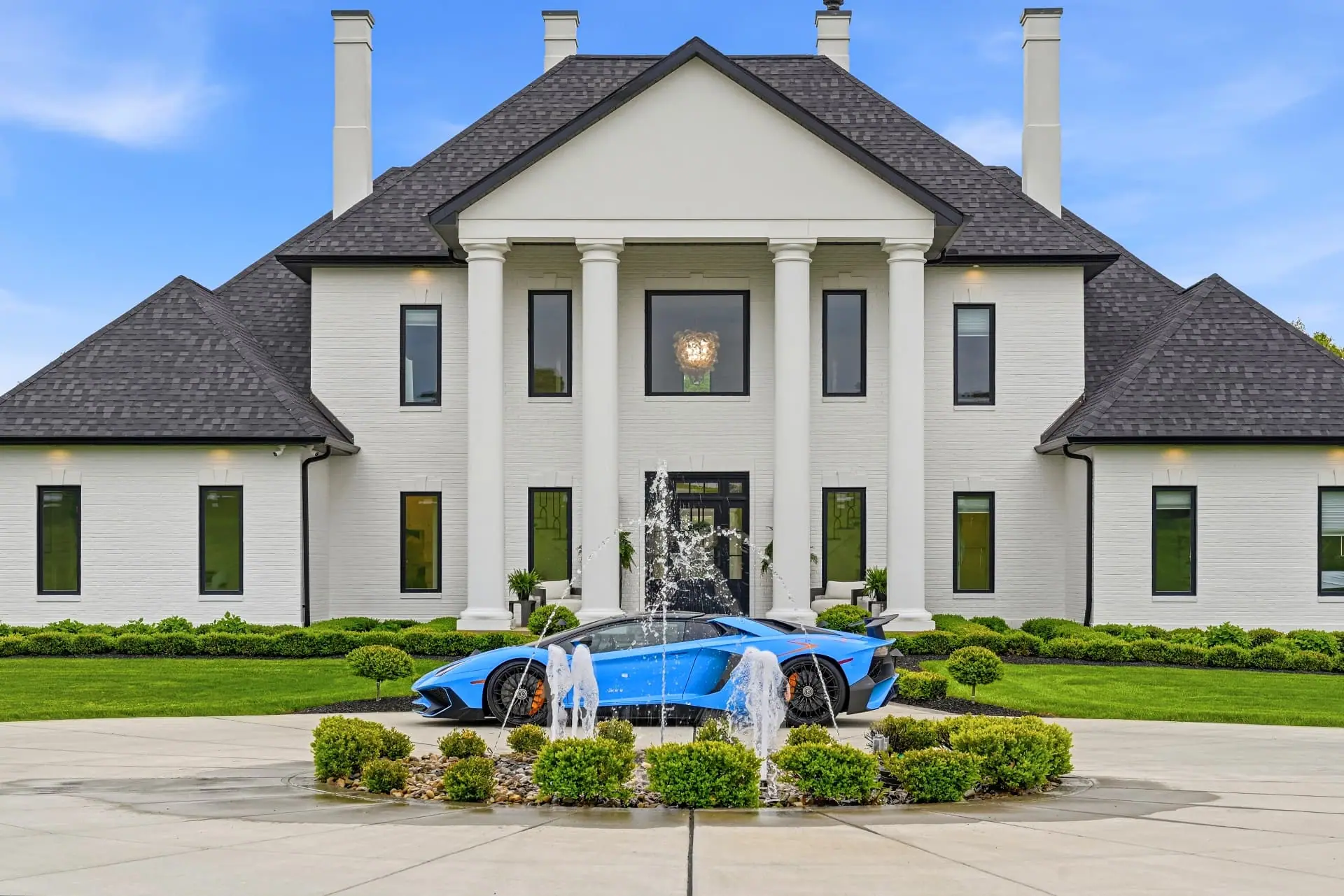 White colonial estate with columns, a front fountain and a blue sports car in the circular drive